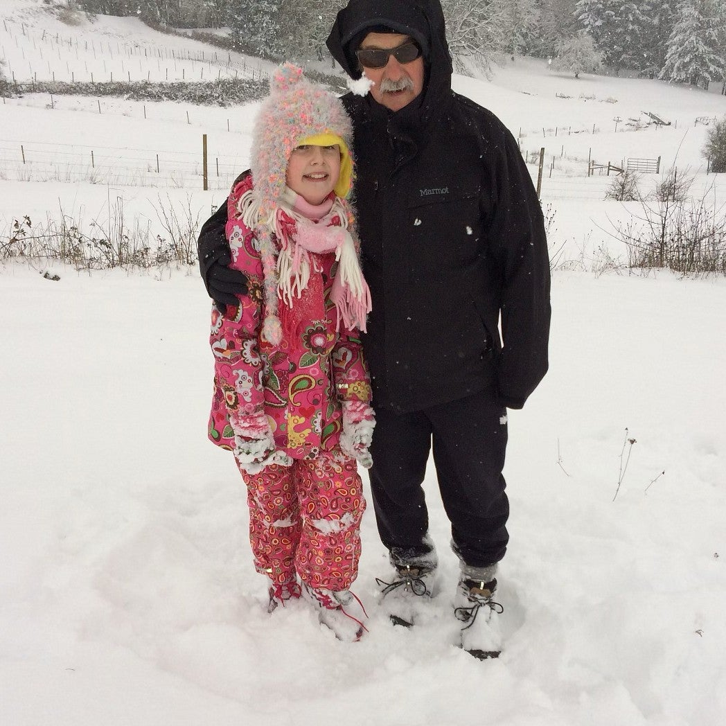 a girl and grandfather posing in winter gear in a snowy field