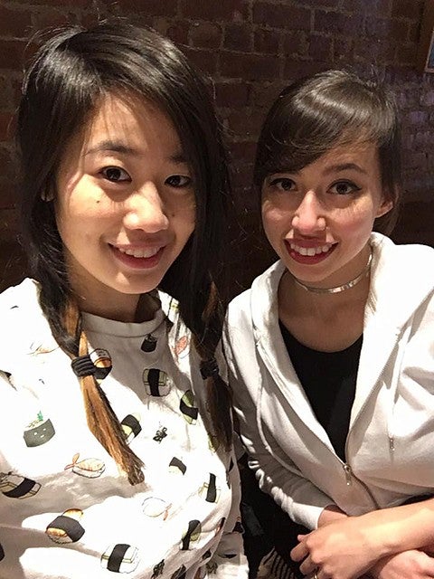 two female students posing for a selfie in front of a brick wall