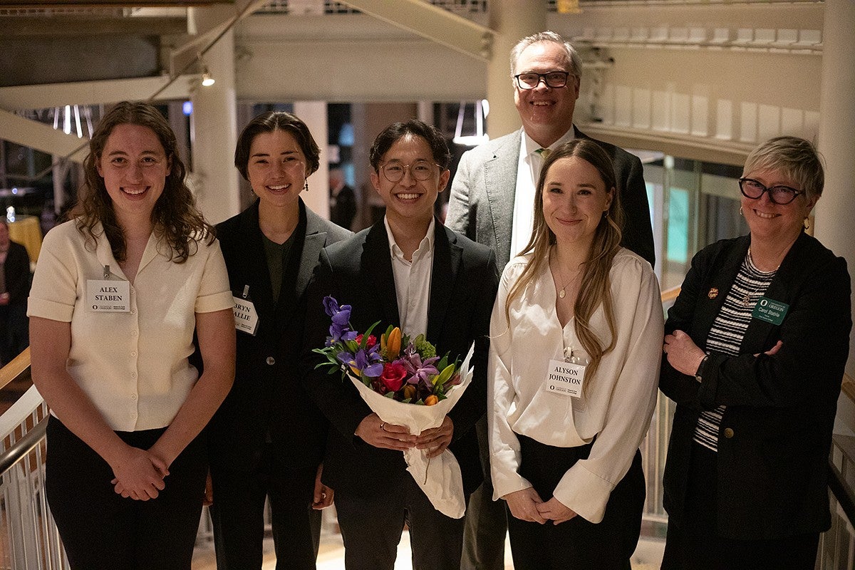 four students posing on lillis atrium steps at night with dean carol stabile and trond jacobsen, one student with a bouquet