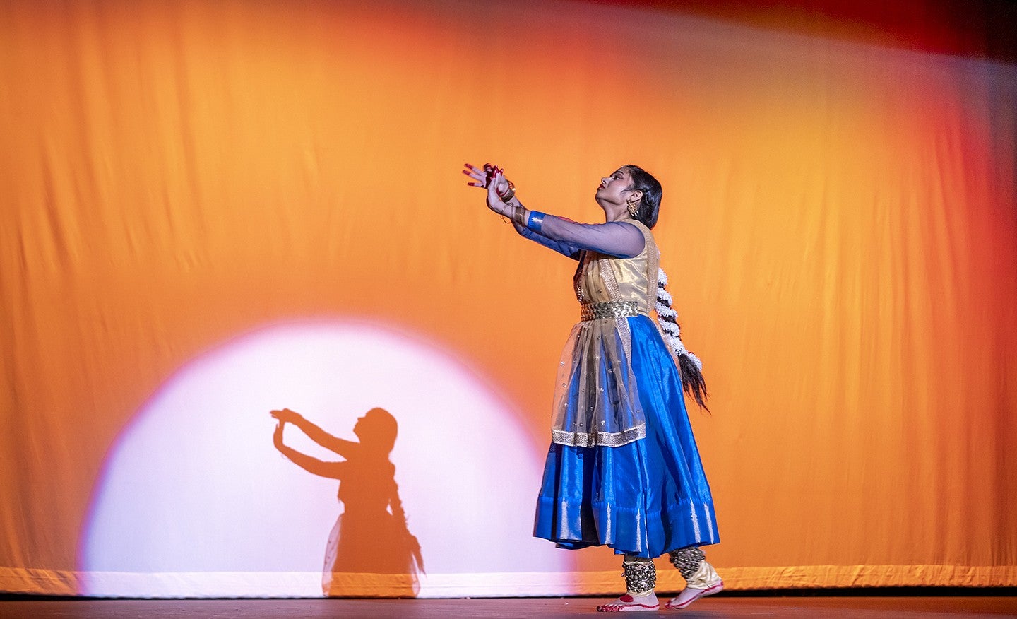 student gayatri misra dancing in traditional indian attire on stage in front of orange background