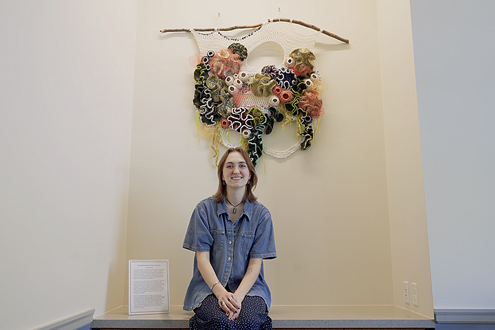 student emma harris sitting in front of her crocheted artwork displayed in Chapman Hall