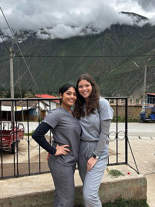 two young women in medical scrubs posing in village street in front of mountainscape