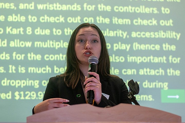 student speaking into mic in front of presentation screen with text about a proposal for nintendo purchase