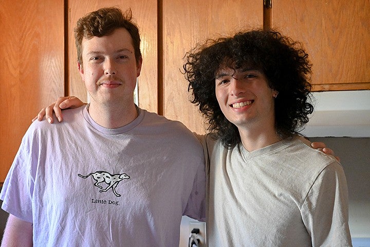 two young men standing arm in arm in kitchen, smiling