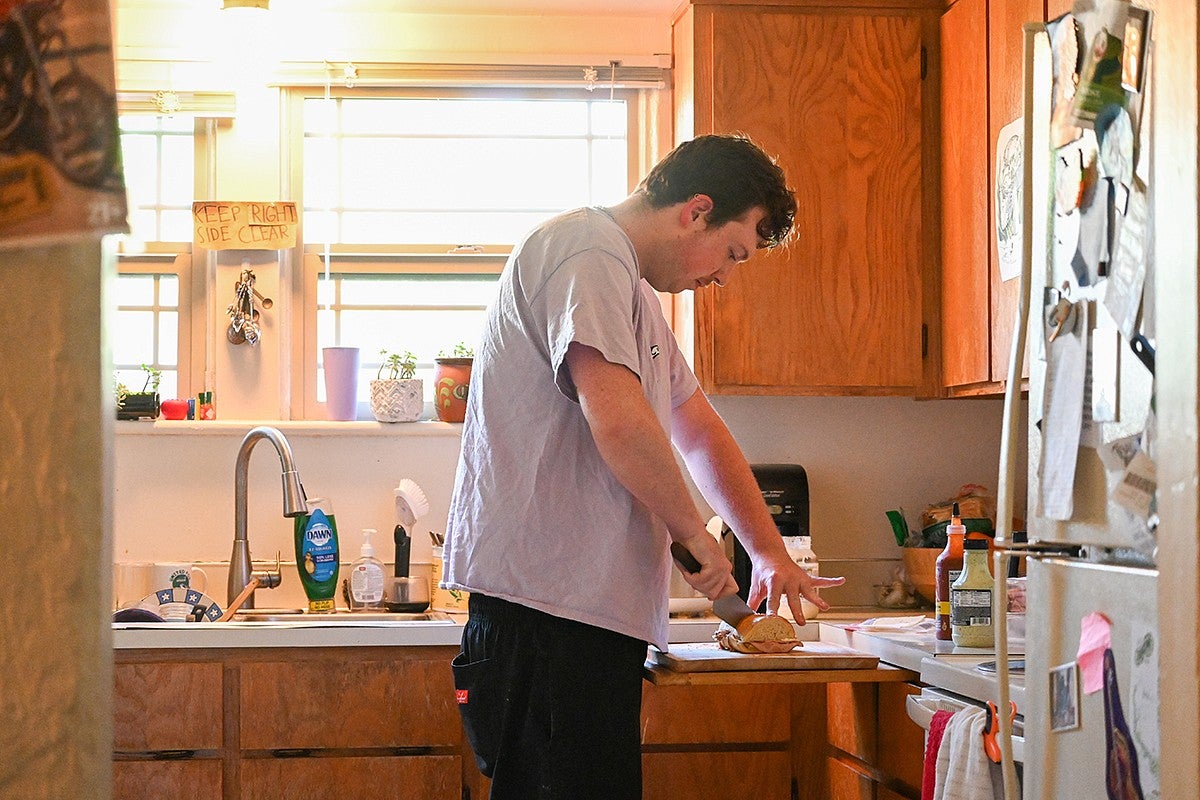 person bending over kitchen counter to cut a sandwich