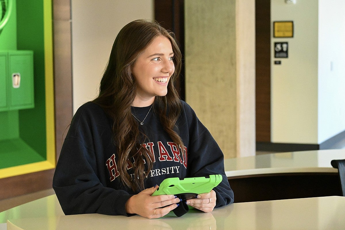 student seated at table in campus building with ipad in hands, smiling off camera
