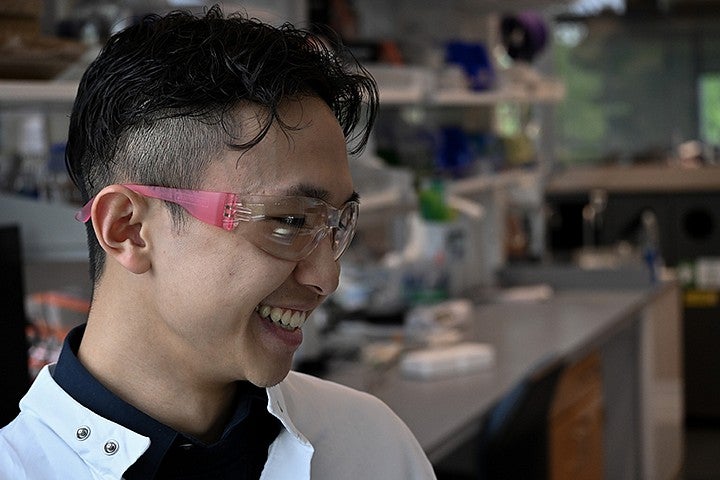 student in lab wearing goggles, smiling off camera