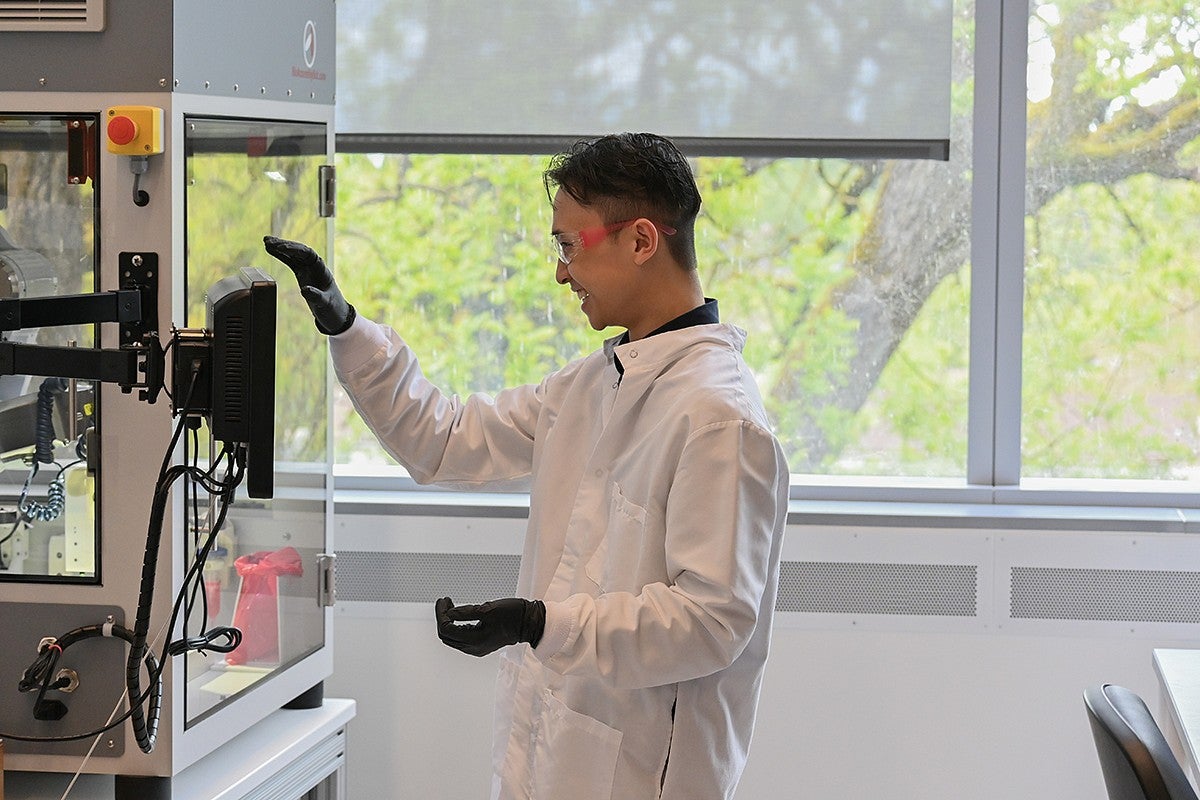 student standing in lab at bench, using equipment