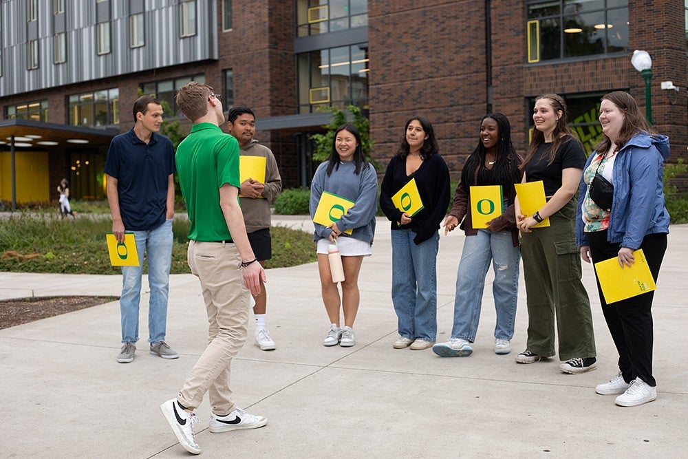 student tour guide in green shirt talking to a group holding yellow folders