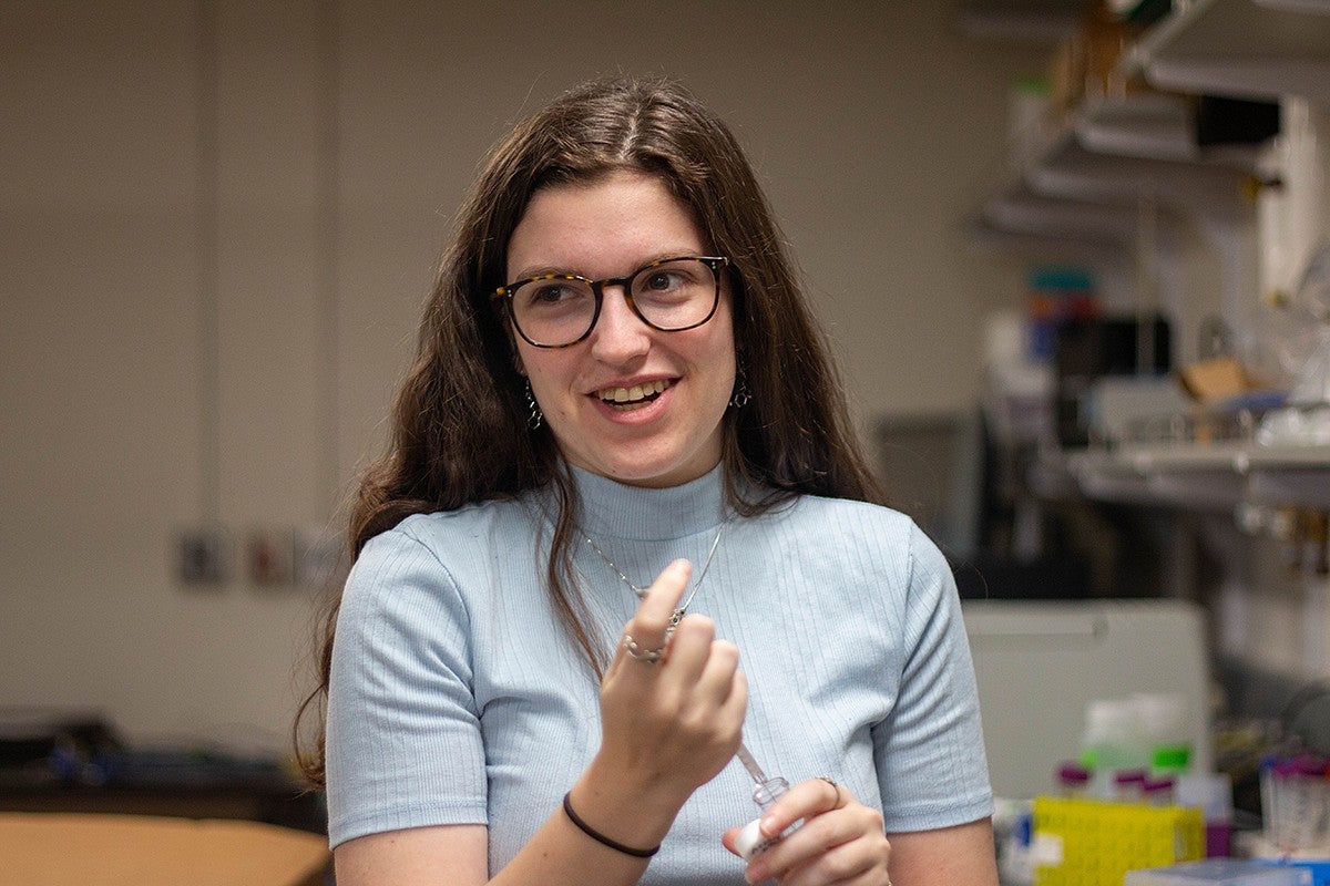 student in lab holding pipette, smiling off camera