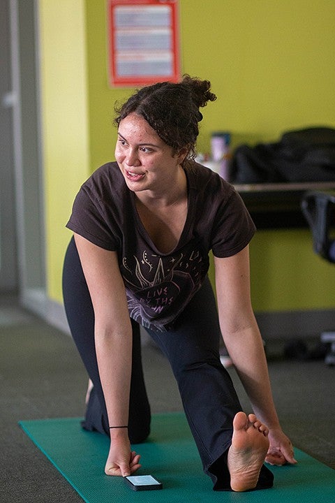 person kneeling on yoga mat, stretching one leg forward and looking to the side, smiling