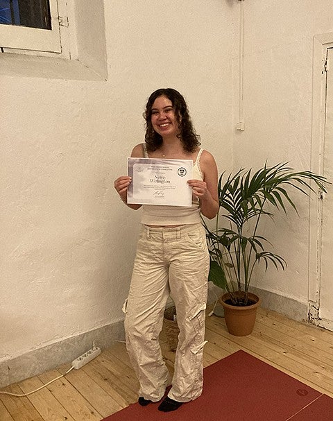 person in white holding certificate of yoga teacher training in studio