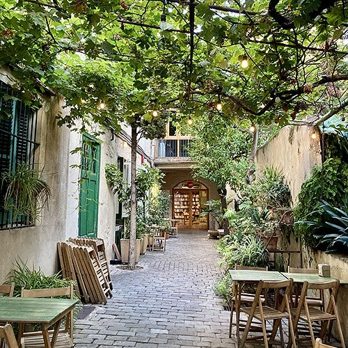 cobblestone courtyard with cafe tables and a green canopy of vines