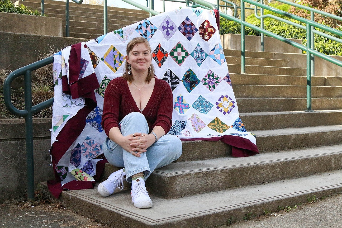 portrait of student sitting on amphitheater steps with colorful quilt draped on railing behind her