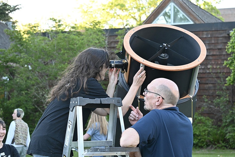 person on ladder peering through large telescope