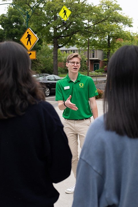student in green shirt talking to tour group on campus and gesturing
