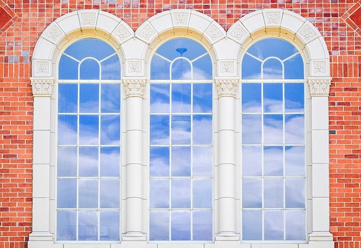 arched windows in a brick building reflecting a blue sky with clouds