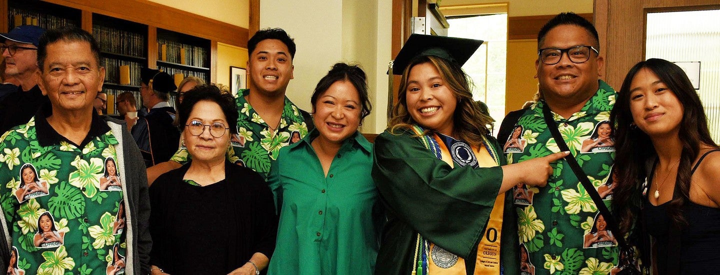 family with graduate in regalia, wearing hawaiian shirts featuring the graduate's photo, in the Chapman Library at the CHC's graduation celebration