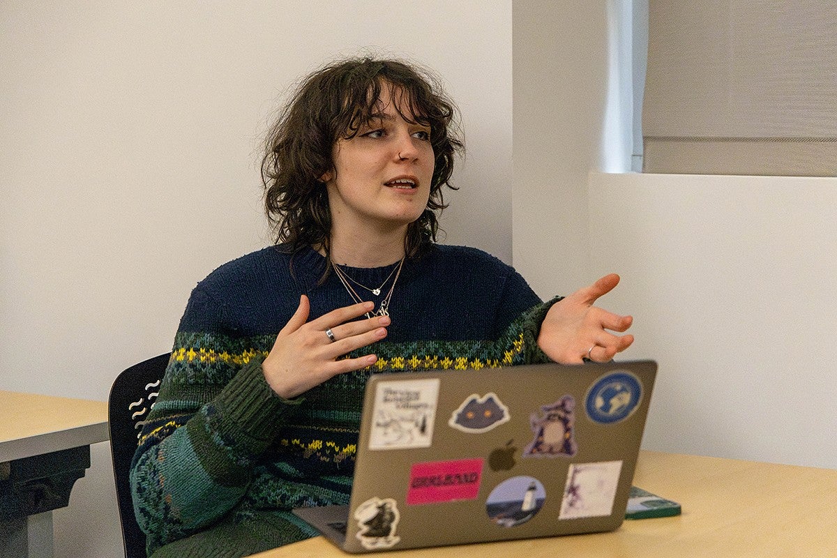 a student, danna rubesh, sitting in a classroom with her laptop in front of her, talking and gesturing