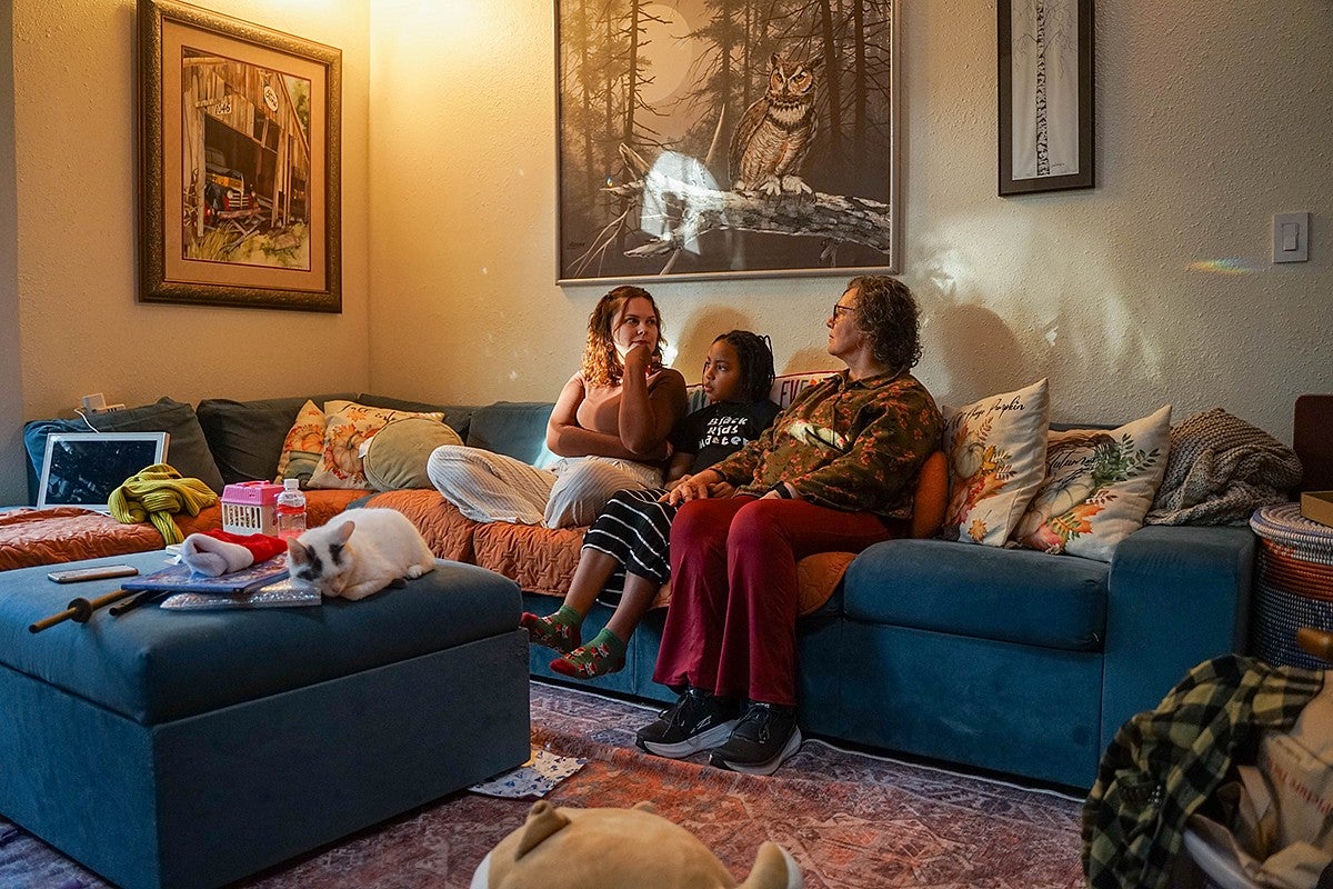 three women and a cat on a couch in a living room decorated with landscape art