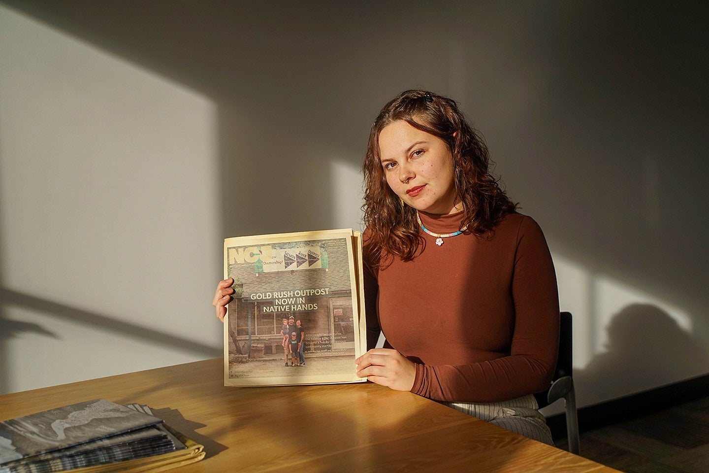 portrait of nika bartoo-smith with a front page newspaper article she wrote with the headline "Gold Rush Outpost now in Native Hands" and a family posing infront of a general store