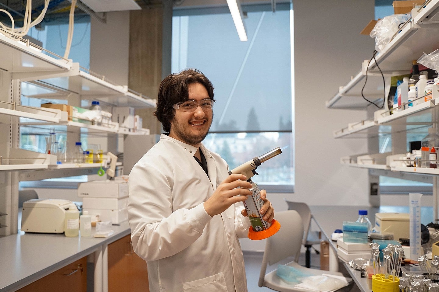 oliver loreto at a campus lab bench, holding a lit blowtorch and smiling