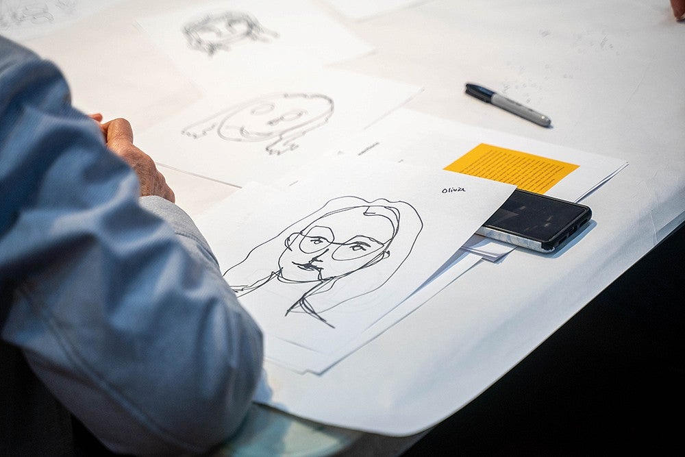 a blind countour drawing of a face in sharpie on white paper, on a table with other drawings