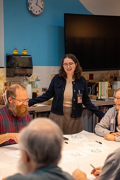 olivia black standing over a classroom table of seniors, talking to them