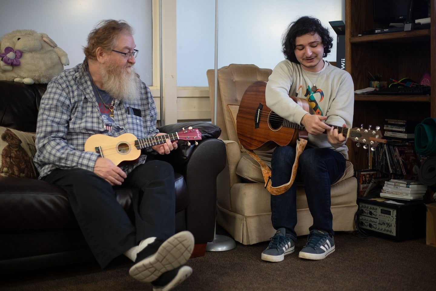 two people seated in armchairs holding a guitar and a ukelele