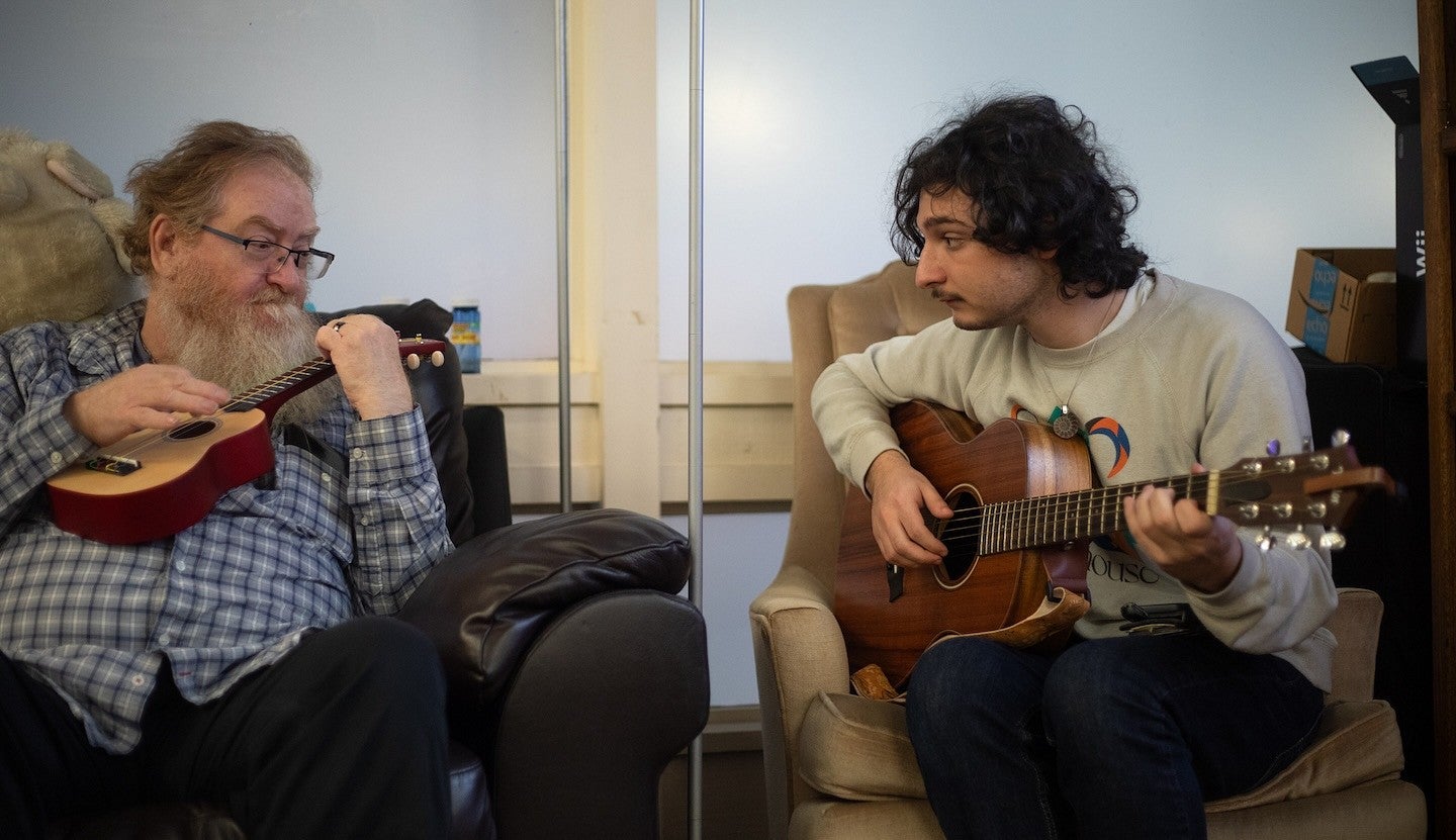 two people seated in armchairs playing a guitar and a ukelele