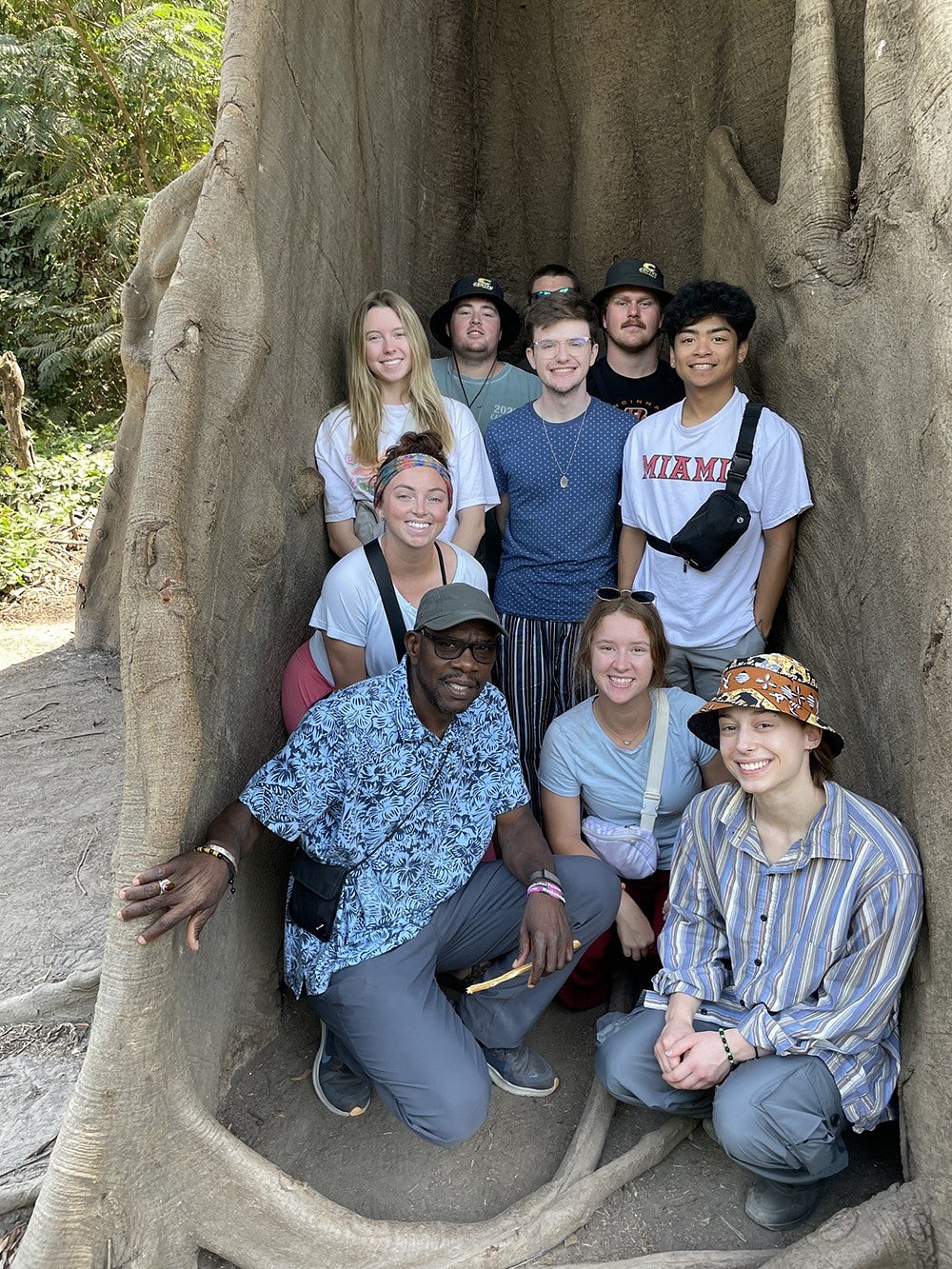 group of students and faculty member huddled between giant tree roots