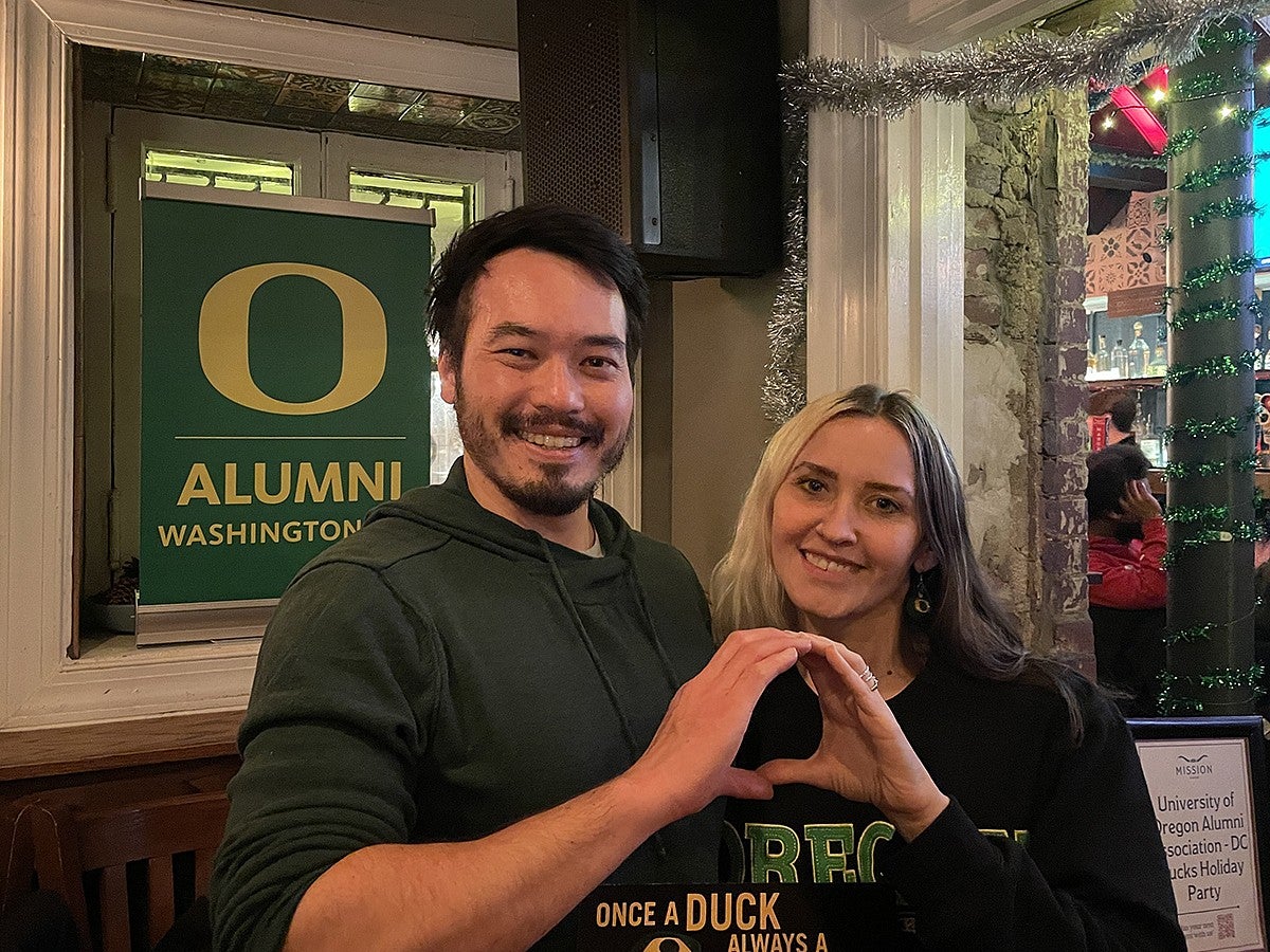 two people arm in arm throwing the O together in front of a UO alumni sign at a party