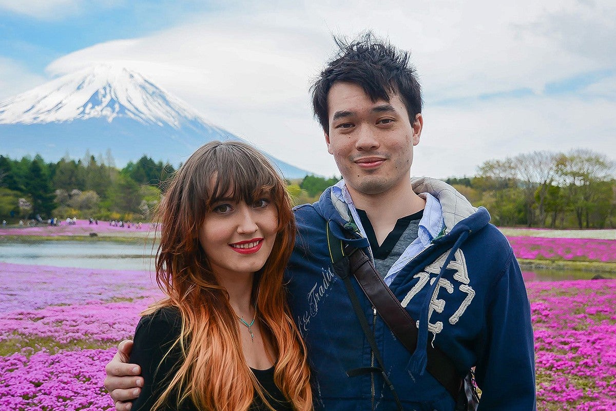 natalie jacobsen poses with her husband in front of a field of pink flowers with Mt. Fuji in the background