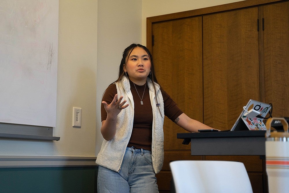 dora ho standing at the front of a classroom, speaking and gesturing