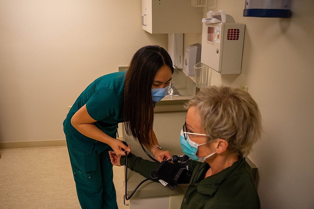 dora ho dressed in scrubs taking a patient's blood pressure with a stethoscope in an exam room