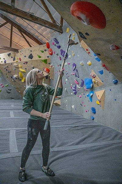 alyssa travis using pole brush to clean chalk off climbing wall grips