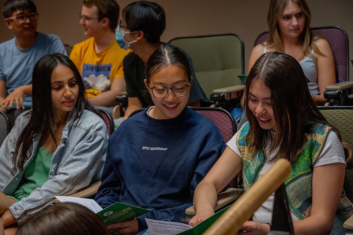 students in audience at three minute thesis looking at program books