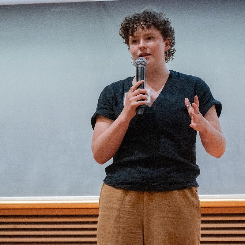 Camila Hess-Neustadt presenting at three minute thesis, gesturing with a mic in her hand