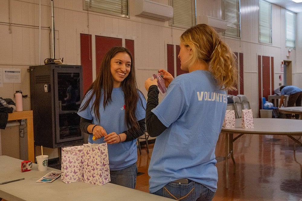 two student volunteers making goody bags on a folding table