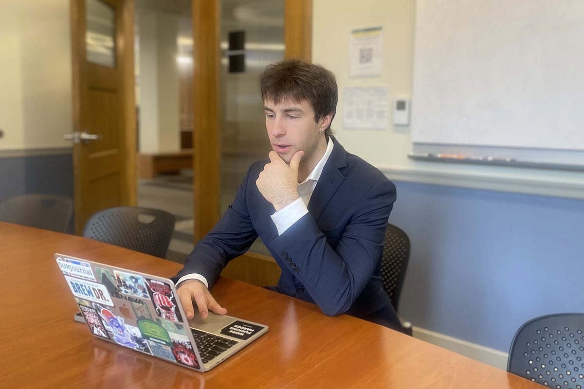 student in suit seated at seminar table on laptop