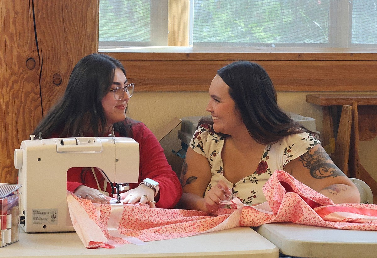 two people smiling together seated at a sewing machine