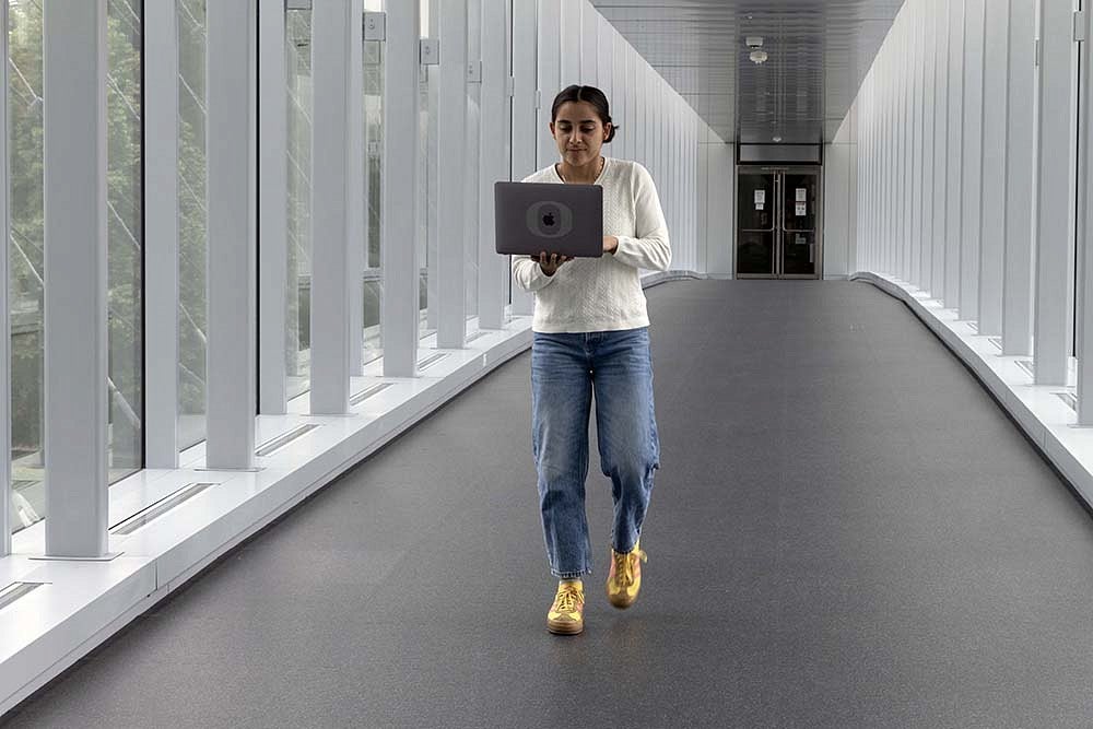 student with laptop walking across knight campus skybridge