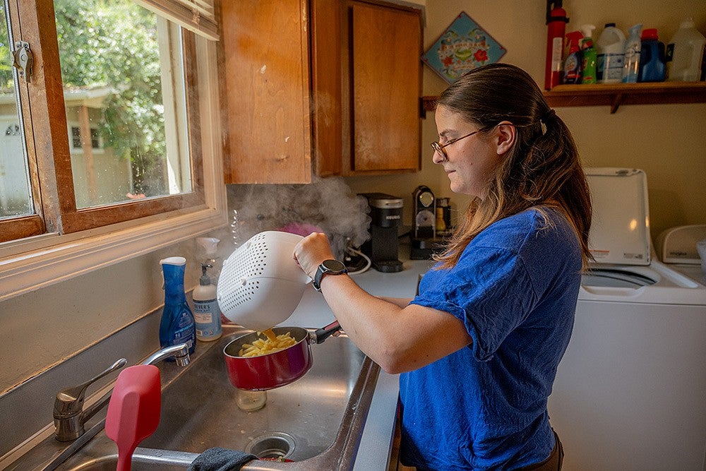 person standing at kitchen sink, draining pasta