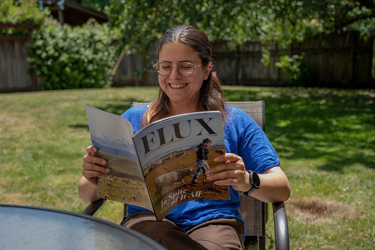 person sitting at backyard table looking through flux magazine and smiling