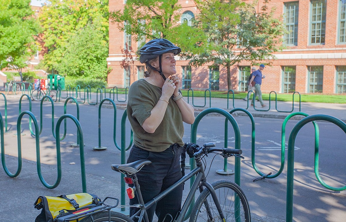 larissa stiglich buckling on her helmet standing at bike on campus