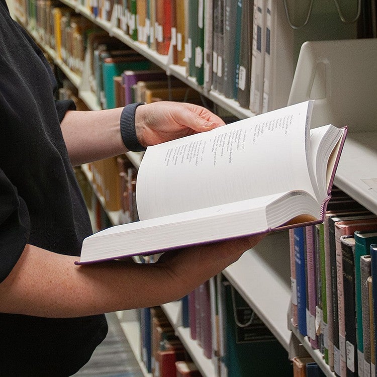 hands holding an open book of poetry among library shelves