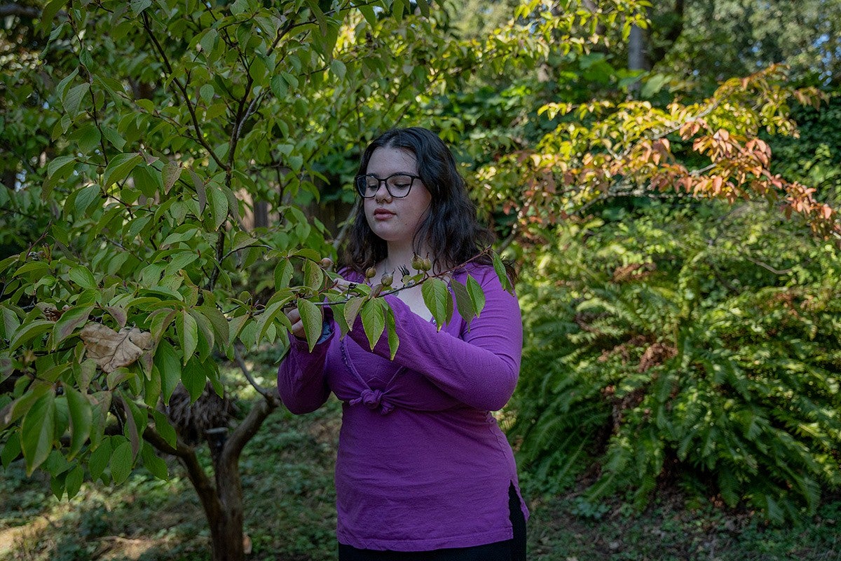 sierra matz examines a tree branch in a park