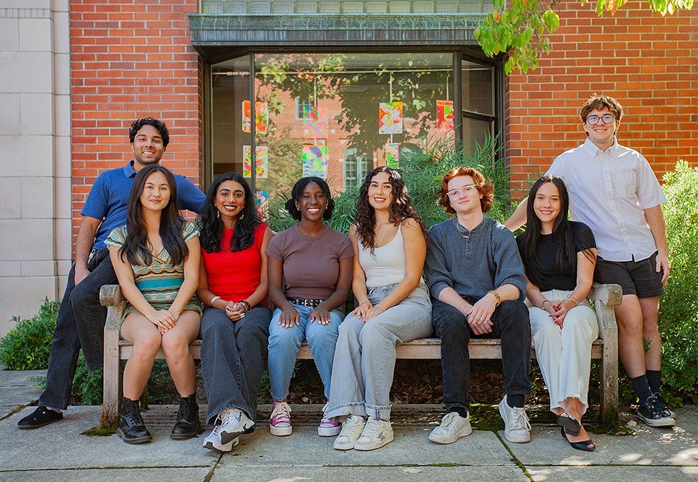 group of students seated on and standing around a bench outside Chapman Hall