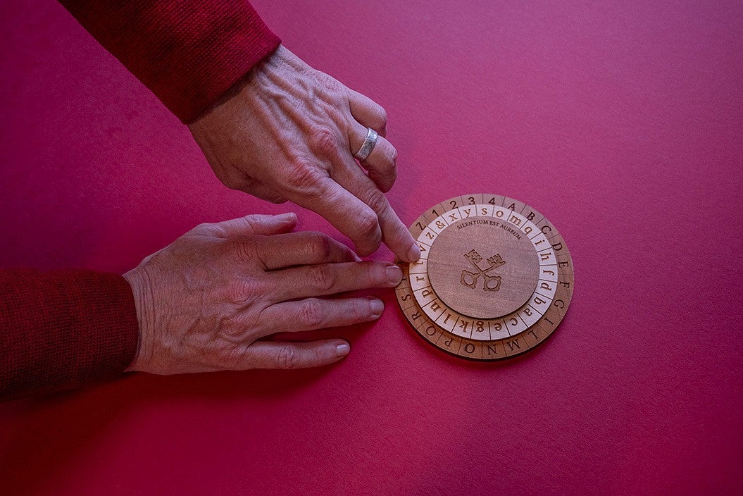 hands using a wooden cipher wheel on a red table