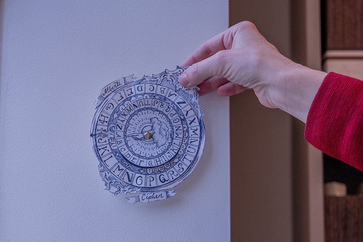 hand holding up a paper cipher wheel on a white wall
